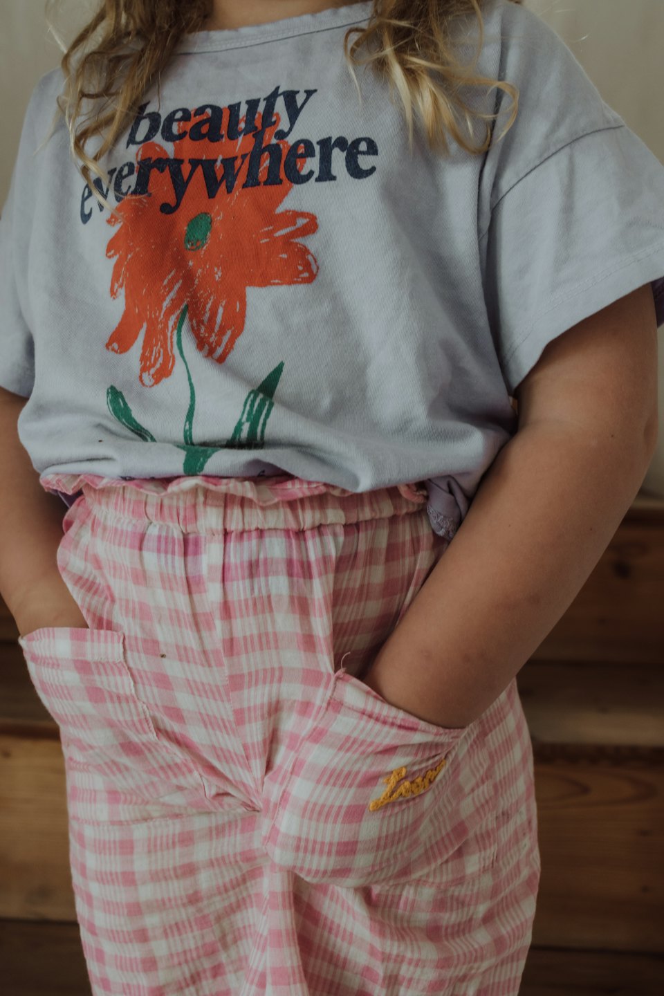 Child wearing a t-shirt and gingham shorts stands with hands in pockets.