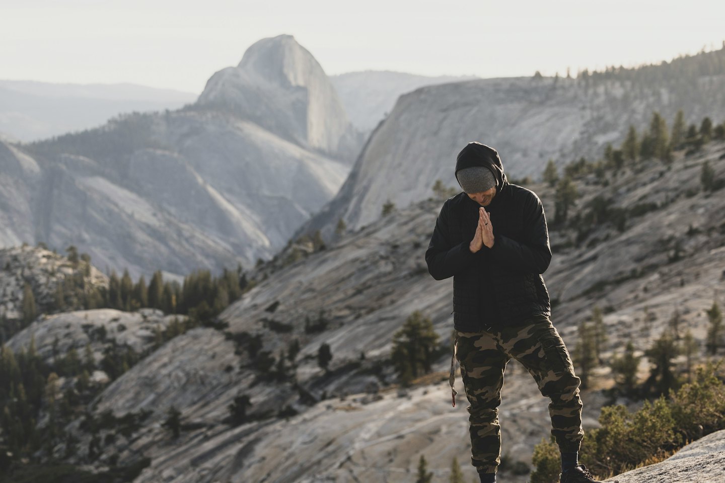 Person standing on a rocky outcrop with hands pressed together.