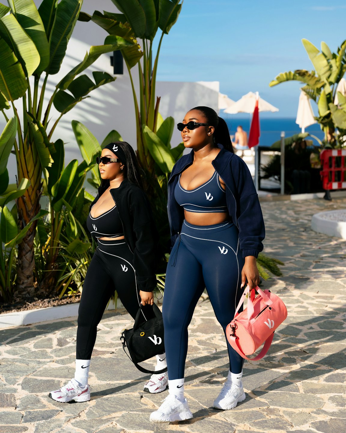 Two women in athletic wear walking past tropical plants.