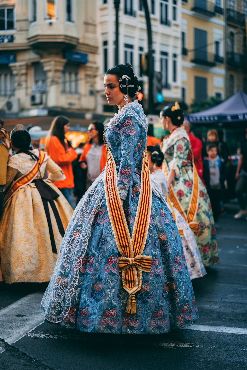 Woman in a traditional blue and gold dress stands on a city street.