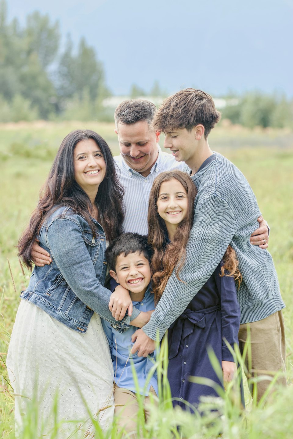 A family of five embraces in a tall grass field.