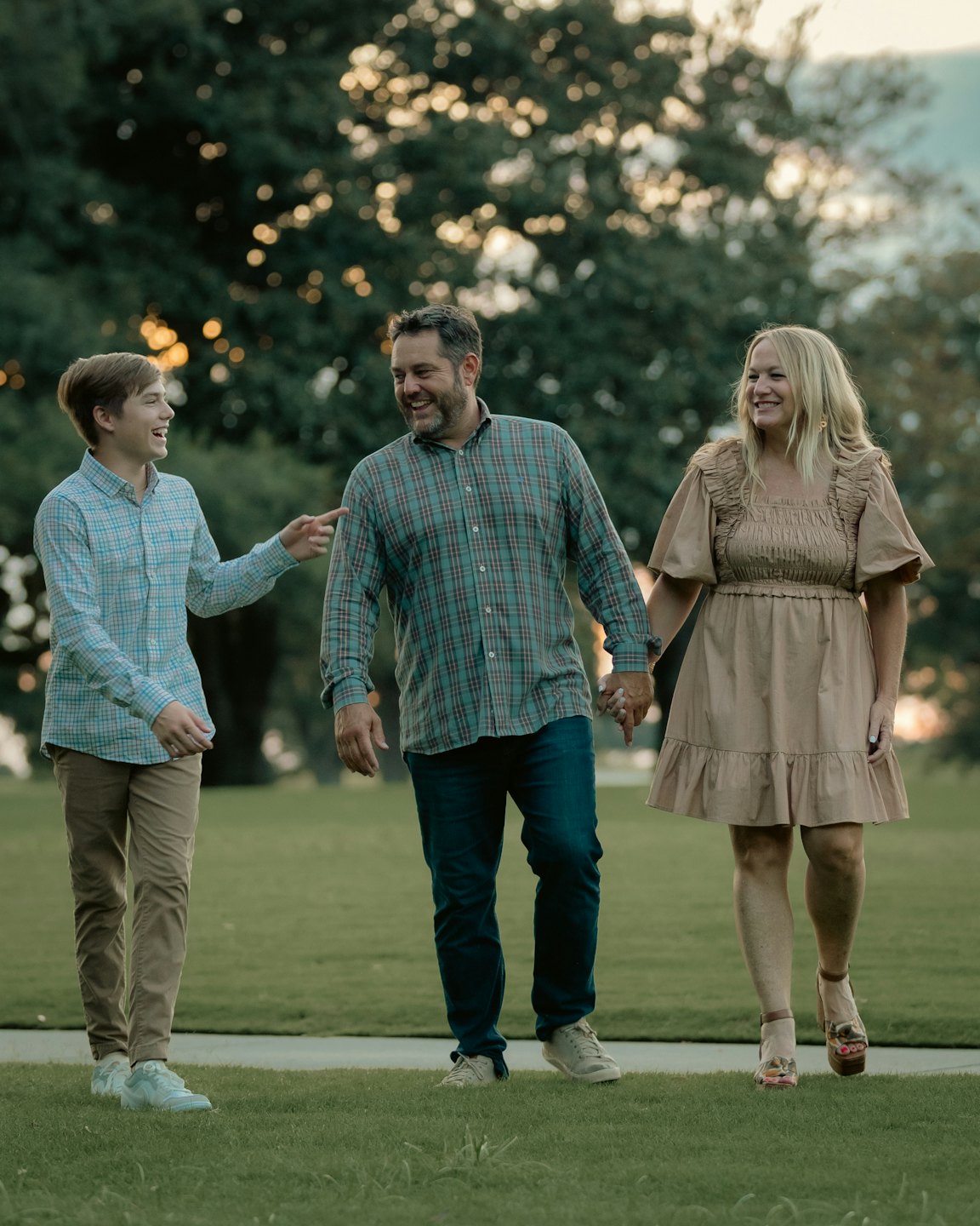 Family laughing and walking together in a sunny park.