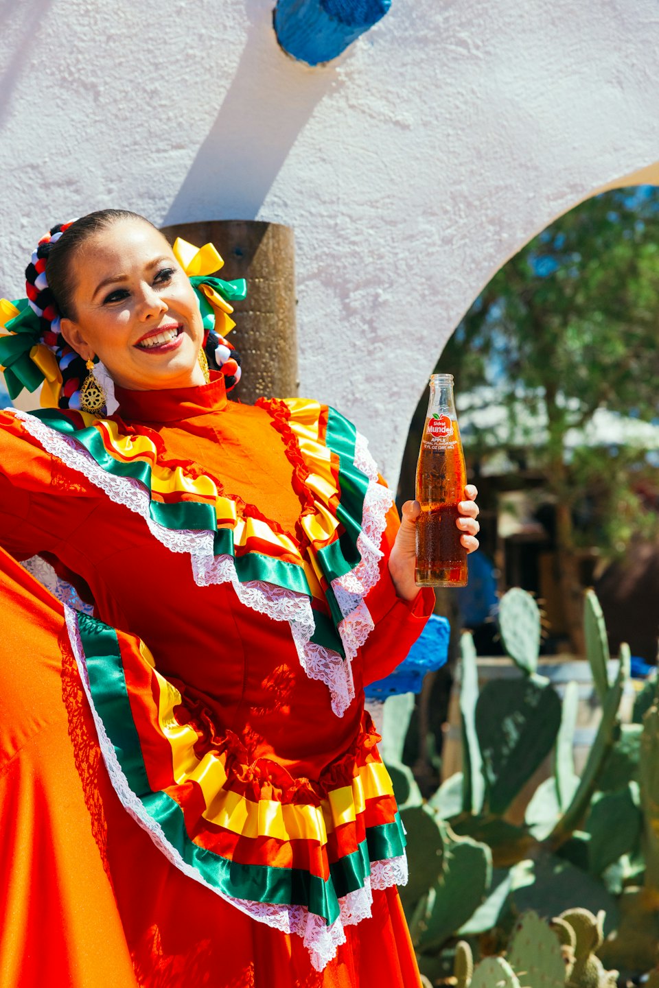 Woman in traditional dress holds a soda near a cactus.