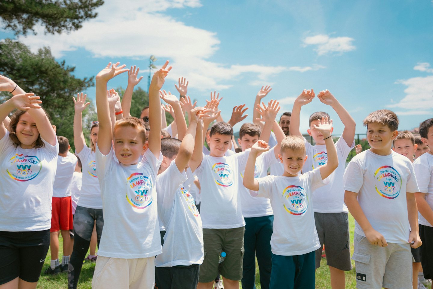 People in matching white shirts raise hands on a field.