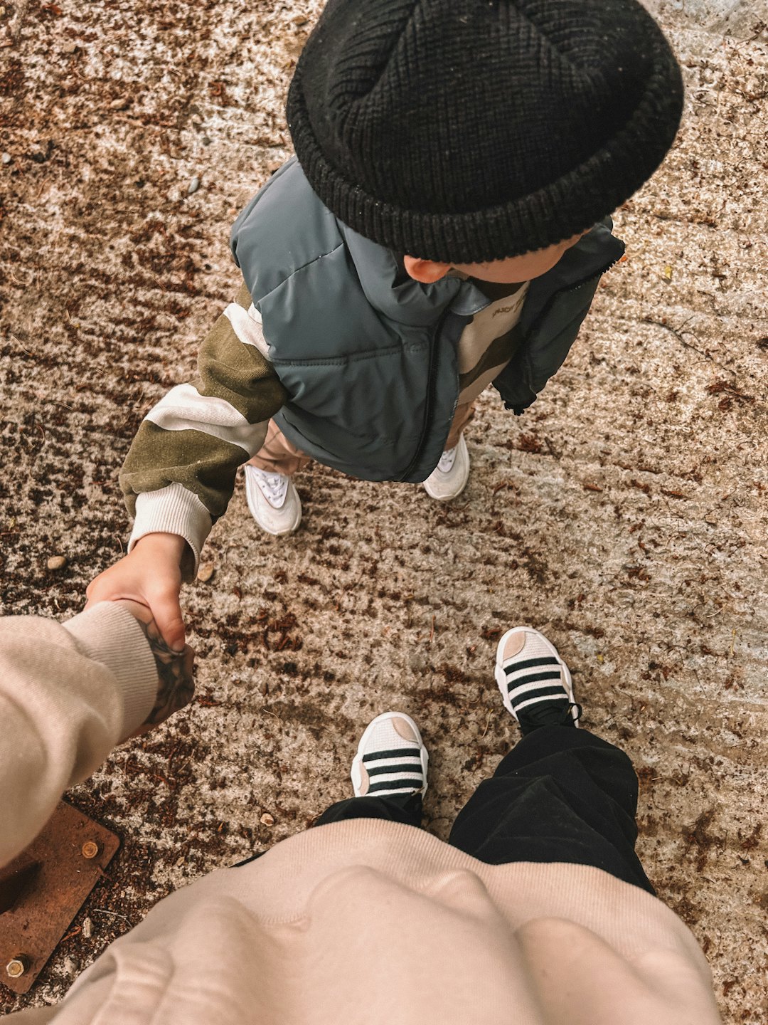 Adult and child hold hands outdoors on textured ground.