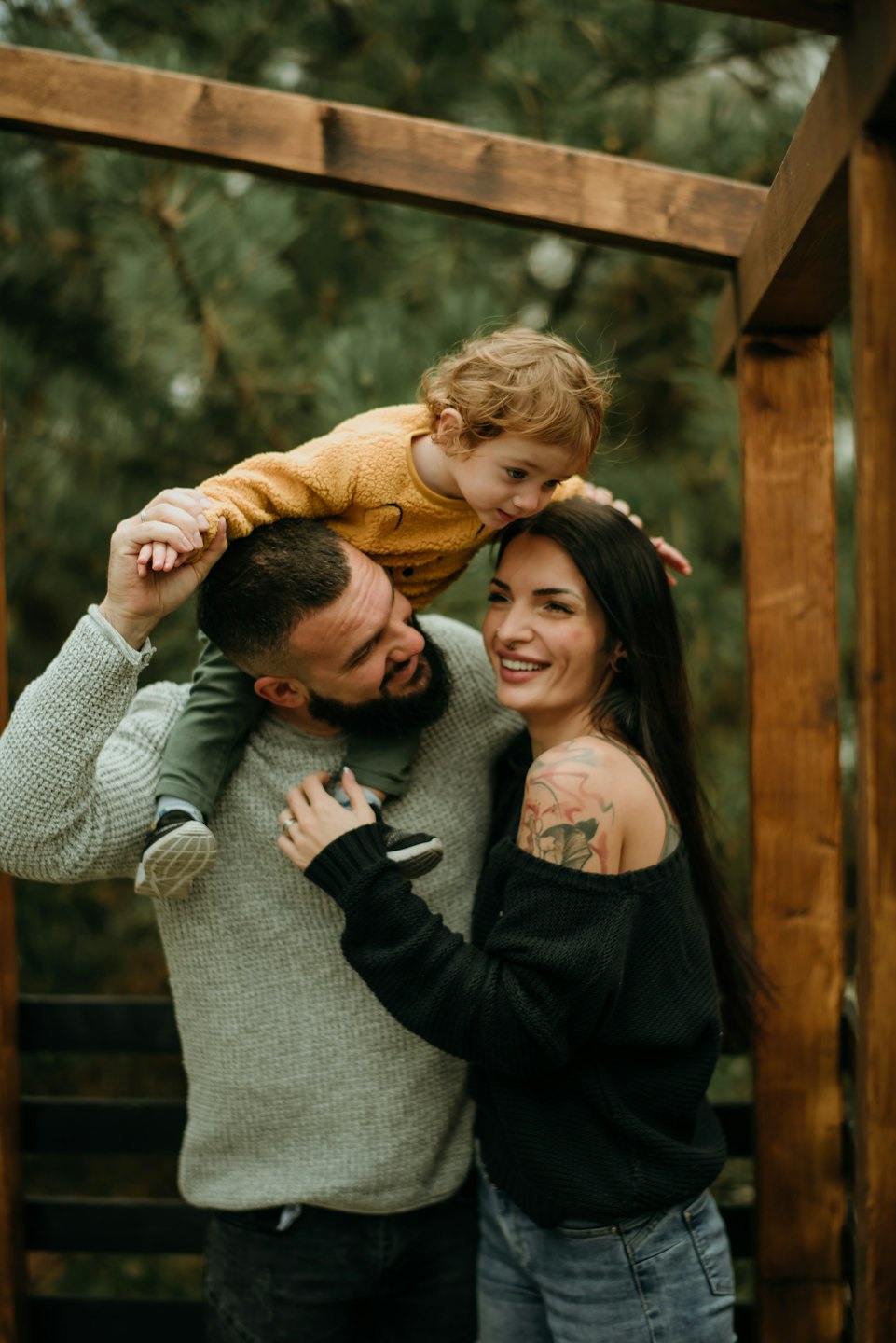 Man carries smiling child on shoulders near smiling woman.